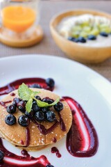 Banana pancakes with blueberries and mint; a wooden bowl of porridge with berries, kiwi, banana and a glass of orange and mango juice in the background - Roxane Cafe, Patong Beach, Phuket, Thailand