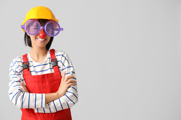 Young female builder with hardhat and funny glasses on white background. Fool's day