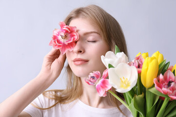 Obraz na płótnie Canvas Pretty young woman with bouquet of beautiful tulips on grey background