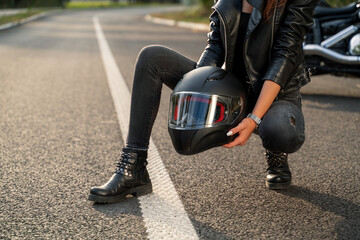 Woman motorcyclist concept, woman holding biker helmet knelling on tarmac 