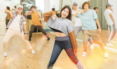 Portrait of cheerful hispanic teenage girl practicing hip-hop movements during group dance lesson in studio.