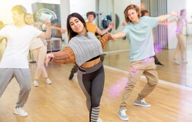 Expressive teen brunette practicing dynamic boogie-woogie in pair with boy during group class in...