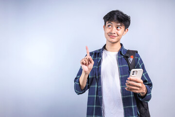 Young Asian college man poiting and looking up to the empty space for ads while holding smartphone