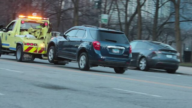 Chicago, IL, USA - February 10, 2023: A dark SUV being towed away down the street in downtown Chicago, Illinois.