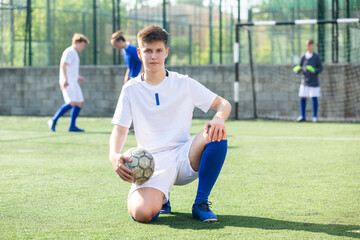 Junior football player sitting on on field with ball
