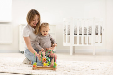 Children toys. Happy mother and her little son playing with bead maze on rug at home, space for text