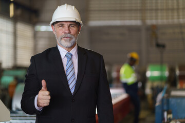 A man in a suit and a hard hat stands in front of a building. He is wearing a tie and a white helmet, show thumb up - obrazy, fototapety, plakaty