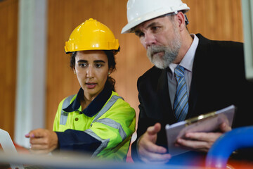 Two people are looking at a laptop, one of them is wearing a yellow jacket. Scene is serious and focused to machine controller board in factory.