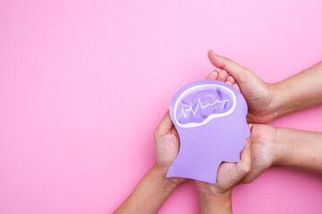 Hands holding human brain paper cutout on pink background.