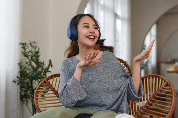 A relax happy woman is sitting on a wicker chair with headphones on.