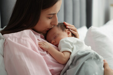 Mother kissing her sleeping newborn baby in bed