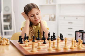Cute girl playing chess at table in room