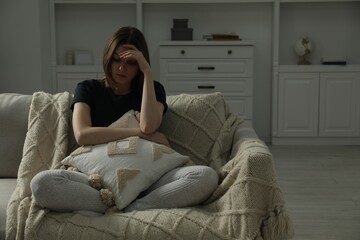 Sad young woman sitting on sofa at home, space for text