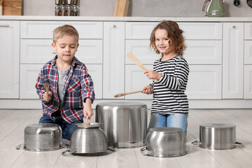Little children pretending to play drums on pots in kitchen