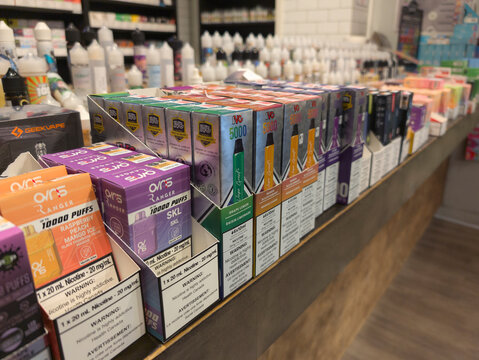 Multiple single use disposable vape  devices and many bottles with different juices for refillable pods at a store showcase. Selective focus. Vape addiction concept.