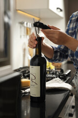 Woman opening wine bottle with corkscrew at black countertop indoors, closeup