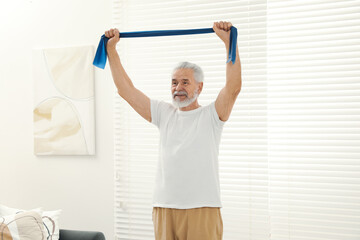 Fototapeta na wymiar Senior man doing exercise with fitness elastic band at home