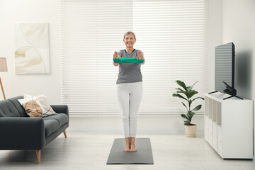 Senior woman doing exercise with fitness elastic band on mat at home