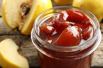 Tasty homemade quince jam in jar and fruits on wooden table, closeup