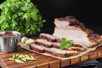Pieces of baked pork belly served with sauce and parsley on table, closeup