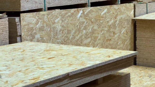 The warehouse of a woodworking factory or hardware store is filled with stacks of chipboard sheets.