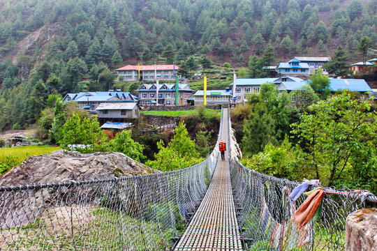 Trekkers on the Everest Base Camp trek pass over steel rope bridges over streams adorned with prayer flags near Namche Bazaar,Nepal
