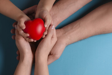 Parents and child holding red decorative heart on light blue background, top view