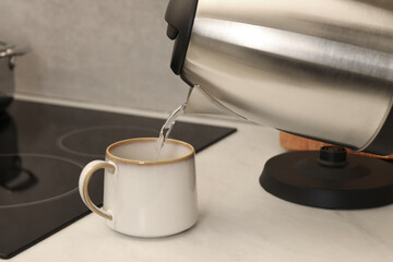 Pouring hot water from electric kettle into cup in kitchen, closeup