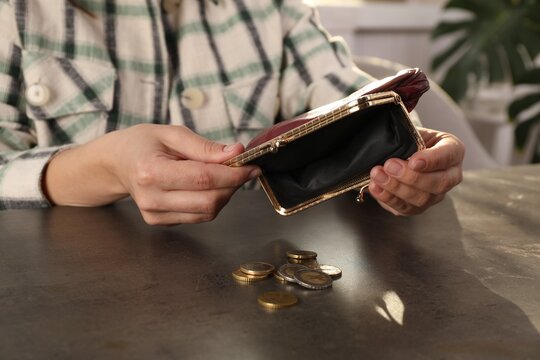 Poor woman pouring coins out of wallet at grey table indoors, closeup