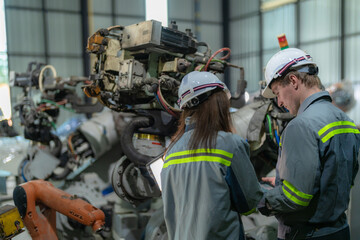 Factory engineer woman inspecting on machine with smart tablet. Worker works at machine robot arm. The welding machine with a remote system in an industrial factory. Artificial intelligence concept.