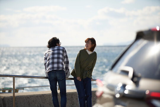 車の向こうで海を見ながら話す男女