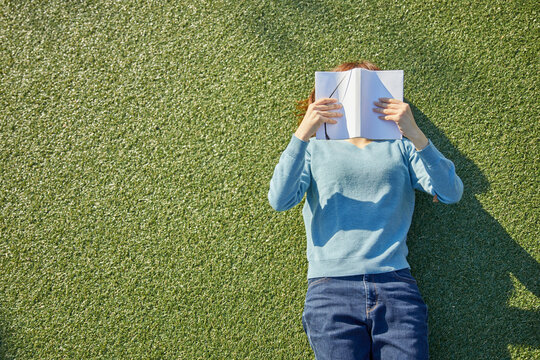 人工芝に寝転んで本を読む女性