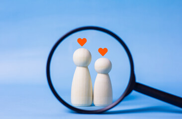 A magnifying glass looks at a male and female wooden doll with a heart icon.