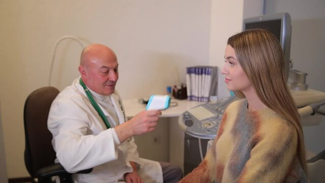 A doctor measures the temperature of a young female patient in a clinic. Concept of diagnosis and treatment