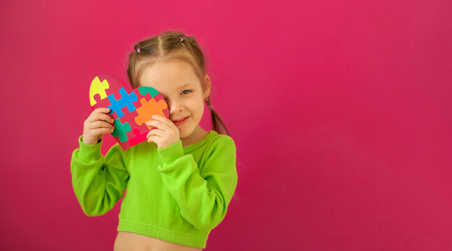 The child shyly covers his face with a heart-shaped postcard made of pieces of cardboard puzzles. Banner in support of people with autism syndrome