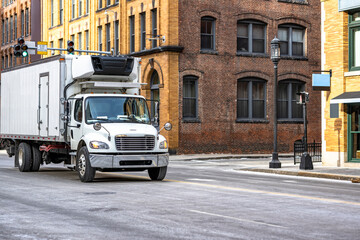 Day cab rig semi truck transporting cargo in long refrigerated box trailer driving on the crossroad...