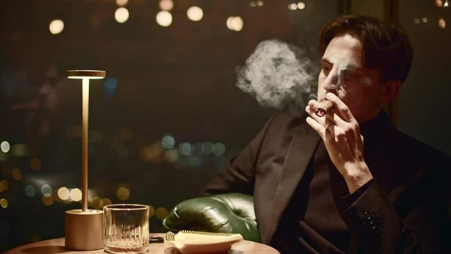 Young man elegantly smokes cigar. Media. Gorgeous man smokes cigar in restaurant. Cinematic cigar smoking in restaurant
