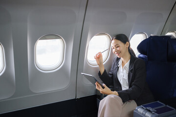 Asian young woman using tablet sitting near windows at first class on airplane during flight, Traveling and Business concept