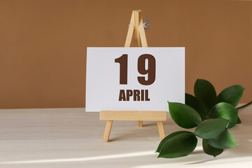 April 19th. Day 19 of month, Calendar date. Green branch, easel with the date and month on desktop....