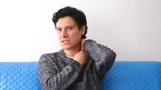 Latino man with tousled black hair feels severe neck pain and makes movements to ease the discomfort