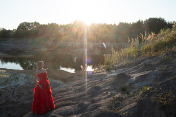 The setting sun's rays cast a radiant glow on a woman in a stunning red dress, poised on a rugged...