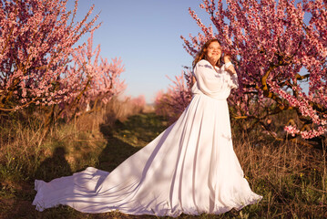 Woman blooming peach orchard. Against the backdrop of a picturesque peach orchard, a woman in a...