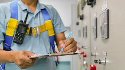 A man is writing on a clipboard while wearing a blue shirt and yellow harness