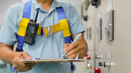 A man wearing a blue shirt and yellow safety harness is writing on a clipboard