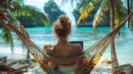 Woman is engrossed in her laptop while lounging in a hammock on a tropical beach, embodying the remote work lifestyle amidst natural beauty.