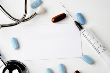 A white card on a white background. Stethoscope, syringe and pills on a white background. Copy space - obrazy, fototapety, plakaty