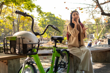 Beautiful woman taking a bike stroll in the park, business woman holding smartphone using bike...