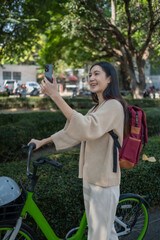 Beautiful woman taking a bike stroll in the park, business woman holding smartphone using bike rental,  business woman holding smartphone using bike rental digital phone