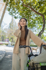 Fototapeta na wymiar Beautiful woman with headphones and smartphone leading a bicycle listening to music, Happy female smiling walk on street with her bike on city road, ECO environment
