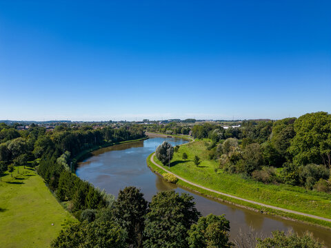 This image offers a splendid aerial view of a meandering river cutting through a lush green landscape under the clear blue sky. The riverbanks are lined with verdant trees and grass, accentuating the